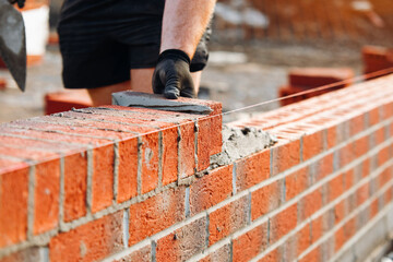 Close-up of bricklayer laying bricks for a new building at a construction site with careful...