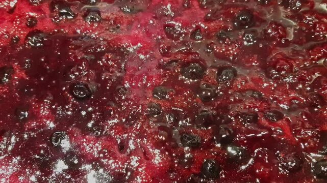 Preparing juicy homemade jam with red and black currants boiling with sugar in a pot.