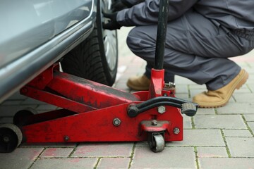 Car lifted by scissor jack. Auto mechanic changing wheel outdoors, closeup