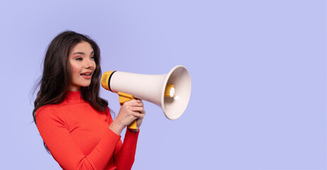 Young woman enthusiastically using a megaphone against  purple background
