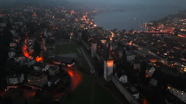Musegg Wall and its nine towers aerial view at night overlooking glowing city in Lucerne, Switzerland. Medieval defenses of Lucerne. Museggmauer Luzern und ihre neun Tuerme Luftaufnahme bei Nacht. 
