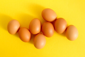 There are many brown eggs lying on a yellow background.