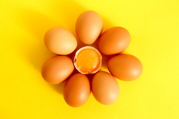 Chicken eggs lie in the shape of a flower on a yellow background.