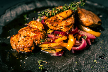 Slice of roasted pork tenderloin with vegetables, pink onion and yellow pepper on a black plate on a dark background. Beautiful, restaurant presentation of the dish.