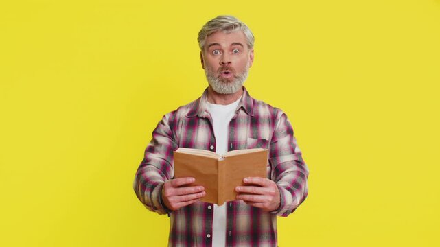 Mature man opens book with eager hope, showing bright surprise and stunned excitement. Middle-aged guy on yellow background shows amazement shocked wow reaction, suggesting hidden intrigue in pages