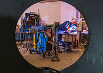 Male worker wearing protective clothing and repair welding sparks industrial construction tank oil inside confined