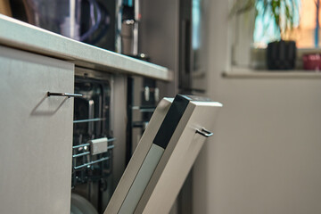 Partially open dishwasher integrated into modern kitchen with natural light. Energy-efficient home...