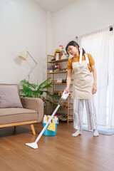 Asian housemaid vacuuming the wooden floor in a cozy living room with cleaning equipment