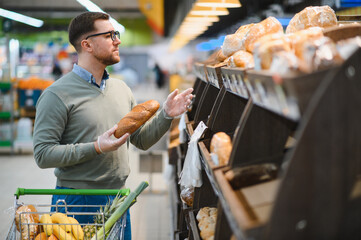 man chooses a fresh bread loaf in the supermarket, in grocery store. man choose food at produce department of shop