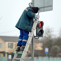Electrician standing on ladder repair traffic light. Man repairing damaged traffic light in city street, equipped with tools and protective gear. Worker maintenance  faulty streetlight at road © Tricky Shark