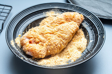 Chicken meat rolled in flour is dipped in egg yolk in a blue plate. French Gordon Blue recipe.