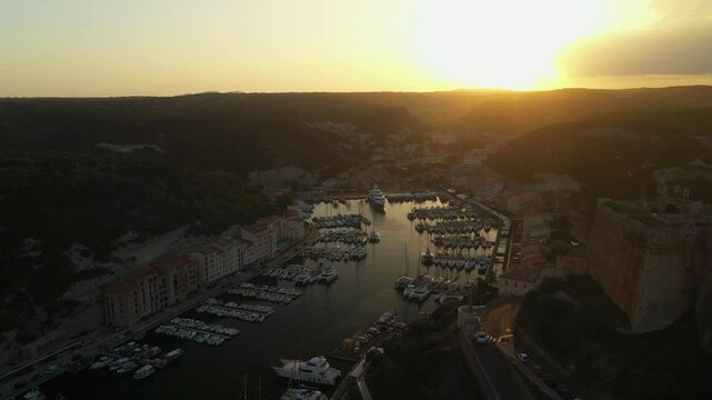 4K aerial video of a sundown over port in an Mediterranean city with a medieval fortress on a rocky hill. City bay with moored yachts and boats with ancient fortress on rocky coast at sunset time 
