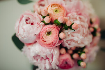A close-up of a romantic bridal bouquet featuring pink peonies, ranunculus, and hypericum berries, creating a soft and elegant floral design.  
