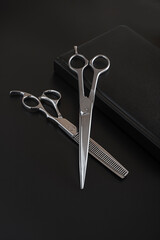 Barber or grooming scissors and notebook diary on black background. Barber or grooming  scissors and daily planner closeup. Hairdresser book for writing 