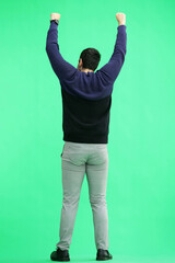 Fototapeta premium A man in a black sweater on a green background raised his hands up, back view