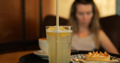 Fresh lemonade glass with meringue tart and cup coffee on table. Woman guest orders tasty dessert and drinks in cafe. Refreshing citrus beverage