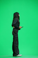 A woman in black clothes, on a green background, full-length, with a phone