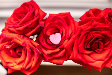 close-up of a single isolated pink pastel candy heart on red roses in a window sill 