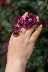 A close-up artistic shot of a woman’s hand adorned with purple flowers, symbolizing natural beauty and creativity. Soft and elegant floral inspiration.