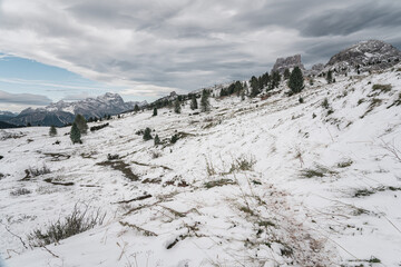 Snow-covered alpine meadows and towering mountains under a dynamic sky. A perfect scene showcasing the raw beauty of winter in the Dolomites.