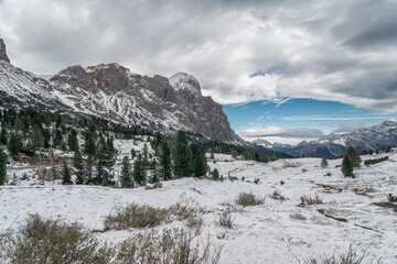 Snow-covered alpine meadows and towering mountains under a dynamic sky. A perfect scene showcasing the raw beauty of winter in the Dolomites.