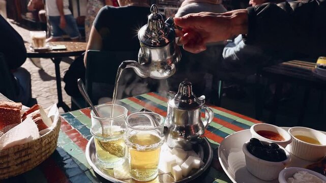 Man's hand close up pouring hot berber tea in the glasses on sunny breakfast cafe Morocco