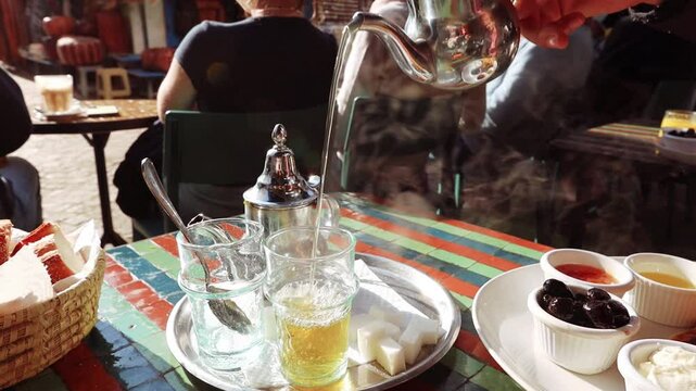 Man's hand close up pouring hot berber tea in the glasses on sunny breakfast cafe Morocco