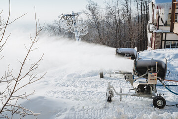 A snow machine is actively blowing artificial snow on a snowy hill, enhancing the winter landscape...