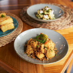 Tahu cabe garam, A vibrant plate features golden fried tofu garnished with herbs, accompanied by other dishes on a wooden table