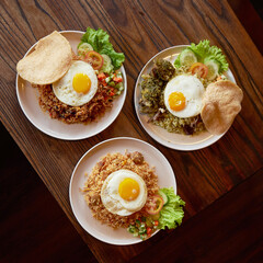 Three plates of vibrant fried rice are beautifully arranged, each topped with a sunny side up egg, fresh vegetables, and crispy snacks
