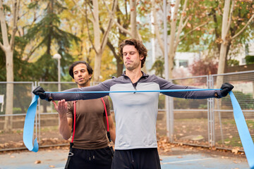 Personal trainer guiding man stretching with resistance band outdoors