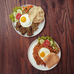 Two breakfast plates showcase perfectly cooked fried eggs, colorful vegetables, and flavorful rice, creating an appetizing display on a wooden table