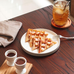 Delicious waffles arranged neatly with chocolate sauce and a refreshing iced drink on a wooden...