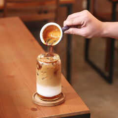 A person pours warm coffee over a glass of ice cream in a modern cafe, showcasing a delightful dessert experience