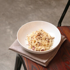 A plate of creamy pasta carbonara topped with cheese and seasoning rests on a soft napkin, showcasing a warm and inviting dining atmosphere