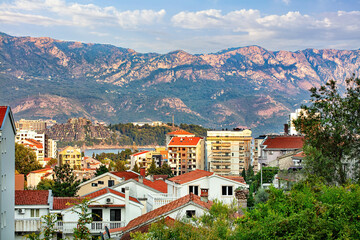 Fototapeta premium Houses of Budva nestled among the hills with a breathtaking mountain backdrop in sunny Montenegro.