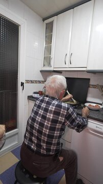 old man alone cooking sitting on stool old man in his eighties in checked shirt
