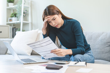 Debt and financial concept, stressed asian young woman have a headache while female calculate expenses, income and expenses, looking bills of credit card for payment or payday on table at home office.