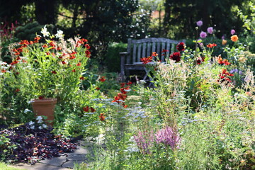 Seat and table in a garden surrounded by flower beds full of heleniums and dahlias in late summer