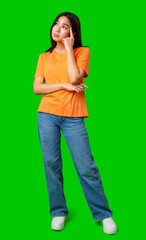 Young woman in orange shirt standing with hand on chin against bright green background
