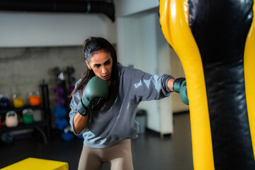 Focused female athlete training with boxing gloves against a punching bag, showcasing strength and...