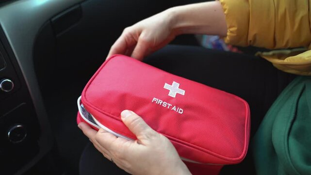 A woman is carefully organizing essential items in a red first aid kit while sitting in a car, emphasizing the importance of preparedness and safety for a secure journey