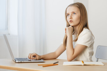 Thoughtful young girl with long hair examines information on laptop, reflecting creativity and inspiration in a bright, modern workspace