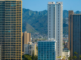 Obraz premium Urban skyline of Honolulu, Oahu, Hawaii, featuring modern high rise buildings in the foreground and lush green mountains in the background.