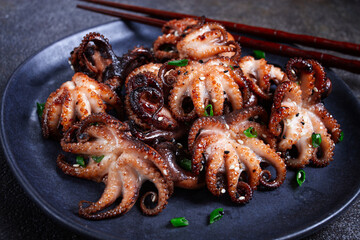 Grilled baby octopus, served with chopsticks, on a black plate, homemade, no people,