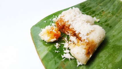 Traditional Indonesian snack called kue putu or putu cake filled with brown sugar and sweet grated coconut, served on a banana leaf and sprinkled with grated coconut on top, on a white background