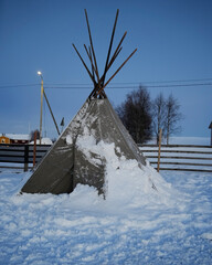 Snow-covered tipi during polar night in Lapland, surrounded by a serene winter landscape. Perfect...
