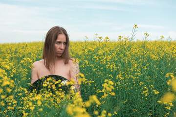 Fototapeta premium A young woman stands in a vast yellow flower field, holding a round mirror. She gazes calmly, blending with the serene natural scenery.