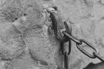 Rusty chain hook attached to a weathered stone wall in an old structure showcasing historical craftsmanship in grayscale