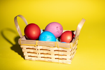 Homemade colored Easter eggs in small wooden basket on the yellow background  ready for Easter